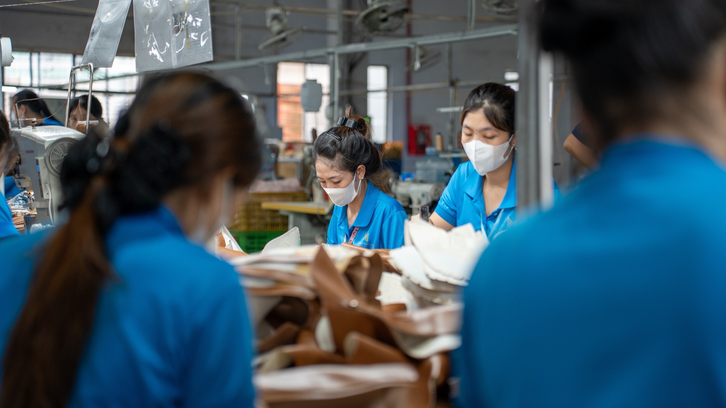 Workers side by side at a cutting table, sorting and inspecting cut leather pieces.