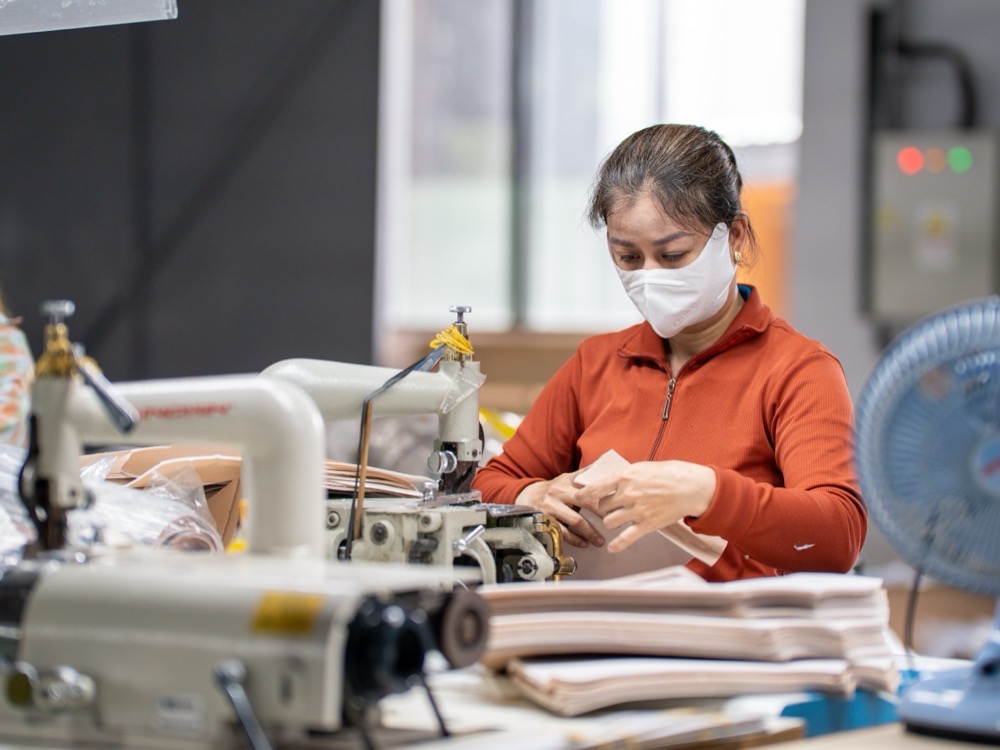 A machinist at a sewing station beside tall stacks of cut panels.