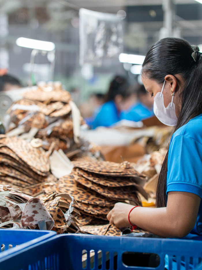 A worker sorting stacks of cut leather panels from a crate at the cutting line.