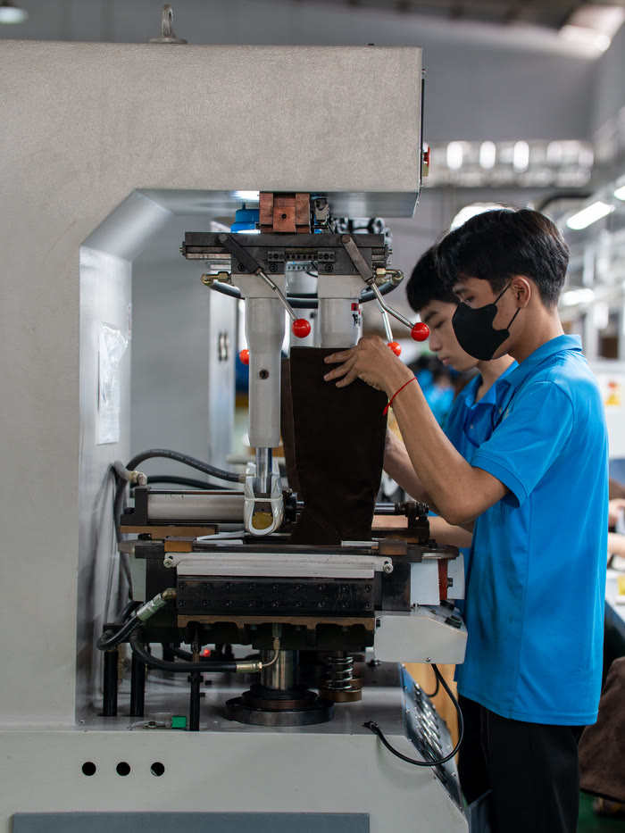 A worker operating a lasting machine that presses a brown leather boot onto its last.