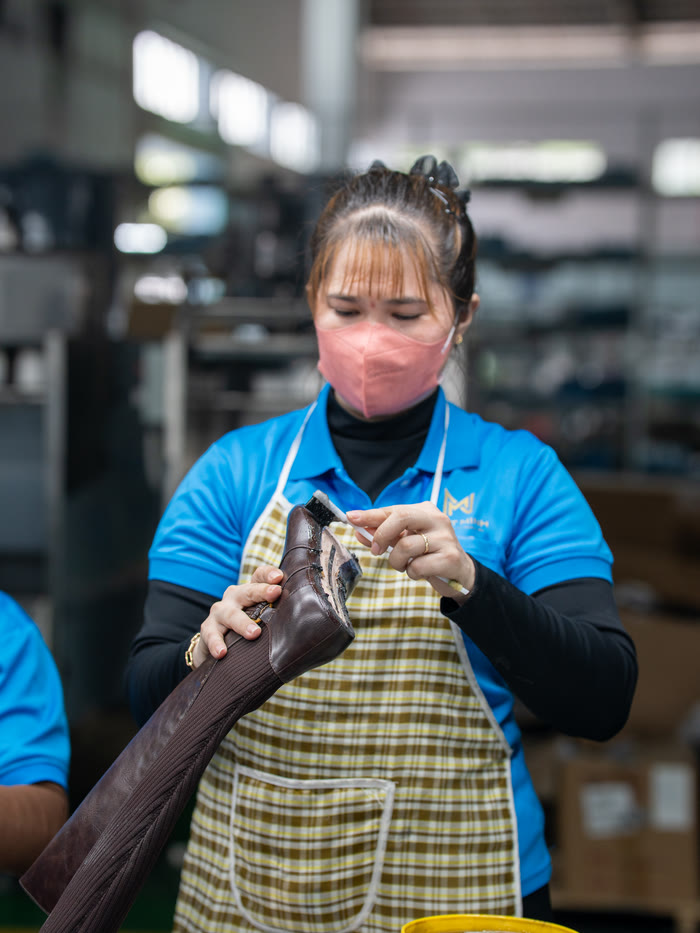 A worker checking the seams of a finished brown leather boot before it is boxed.