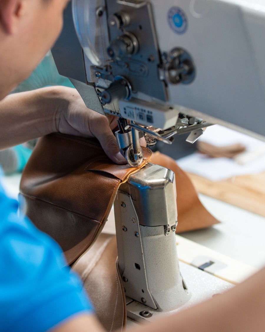 Close view of a machinist's hands feeding a tan leather upper under a stitching needle.