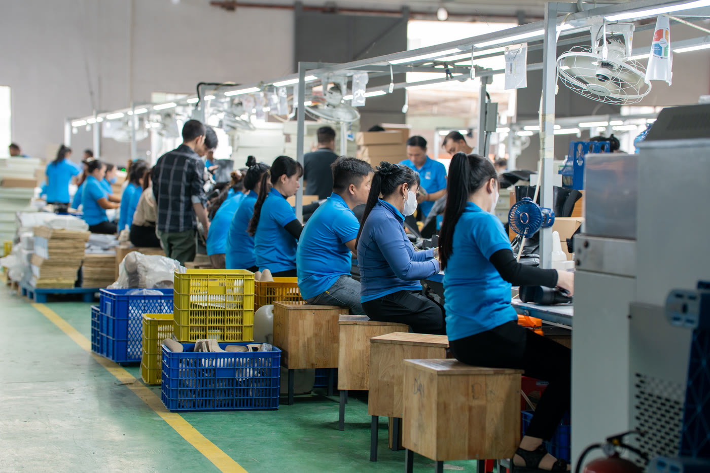 A wide view of the production floor, with benches and workers running away down the length of the hall.