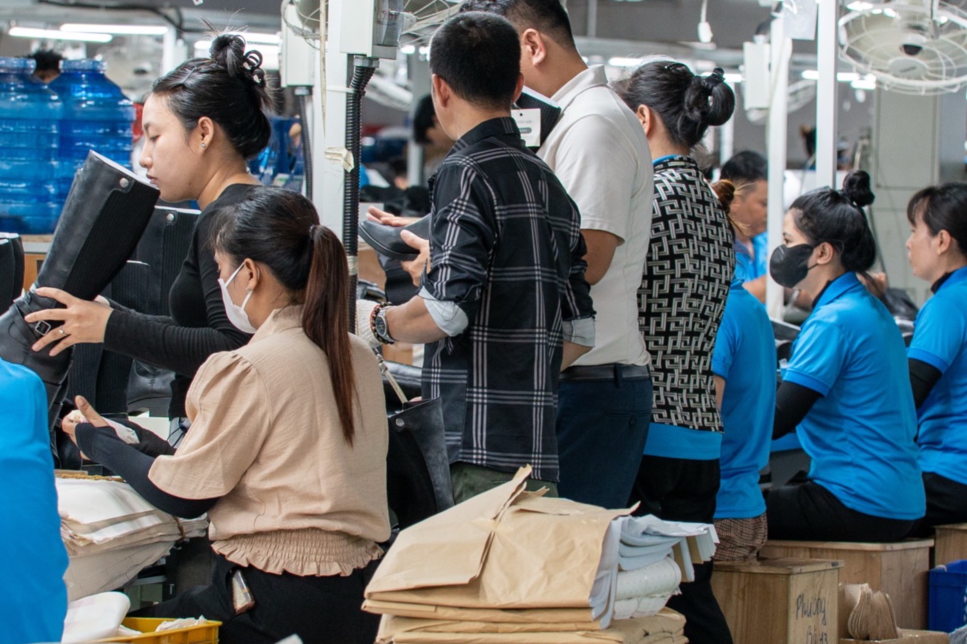 Workers standing shoulder to shoulder at a bench, wrapping finished pairs in paper.