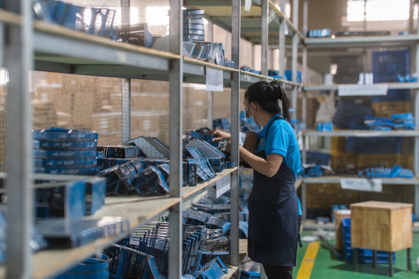 Steel racking holding trays of blue lasts, with a worker lifting one down.