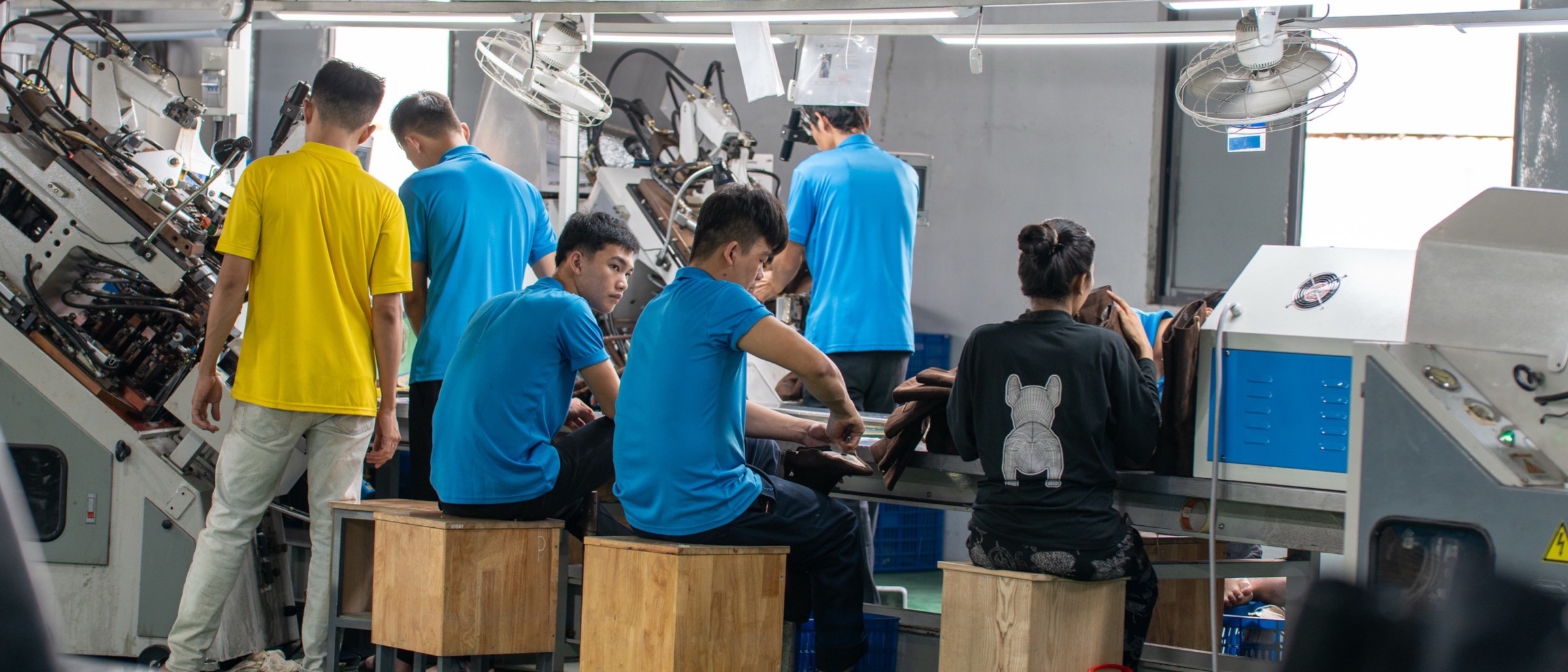 A row of colleagues seated at the assembly line, machines running the length of the bench behind them.