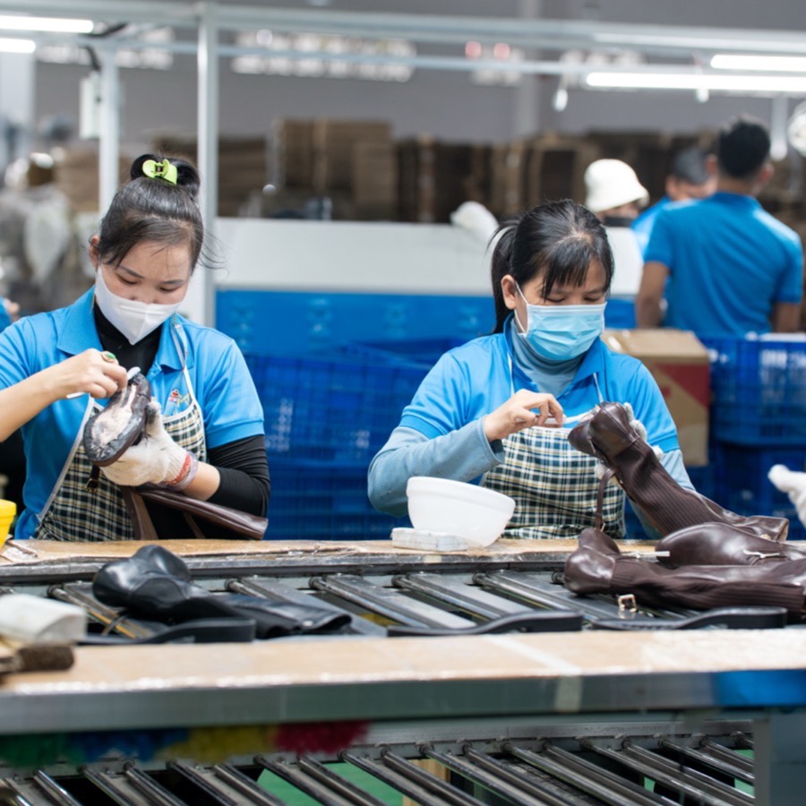 Two workers in aprons cleaning dark leather boots at the conveyor.