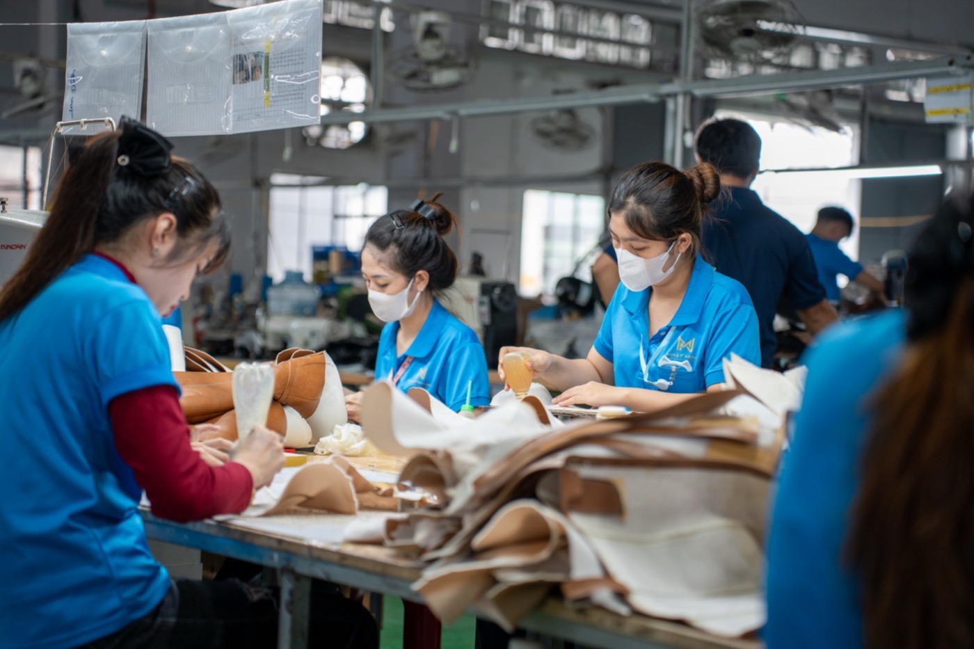 Workers at a long bench sorting cut tan leather panels beside stacked hides.