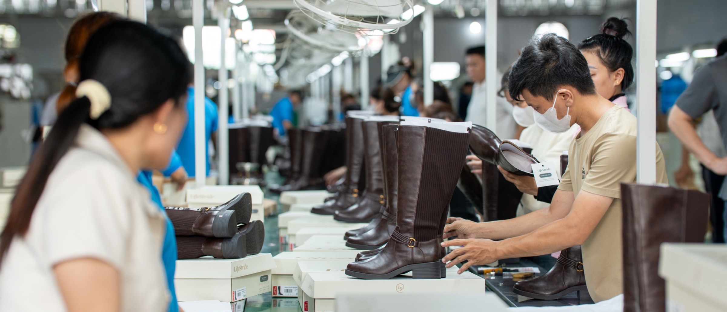 Tall brown leather boots standing in a row along the finishing line, with boxes stacked beside the bench.