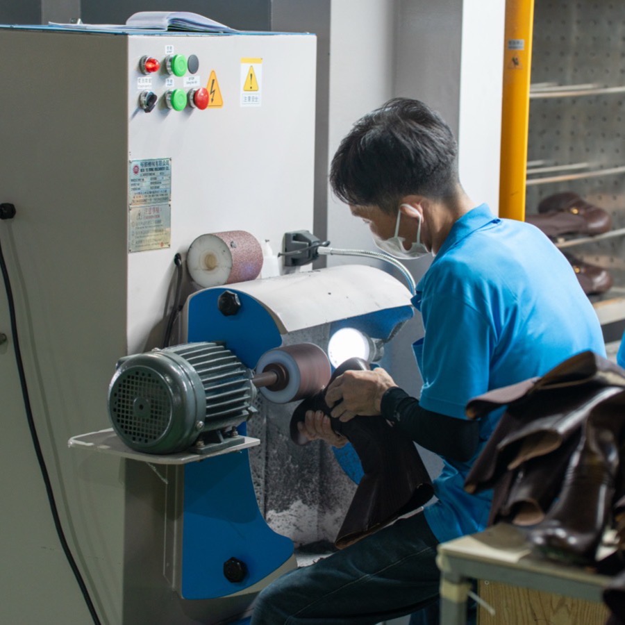 A worker roughing the lasted edge of a dark upper against a wheel before cementing.