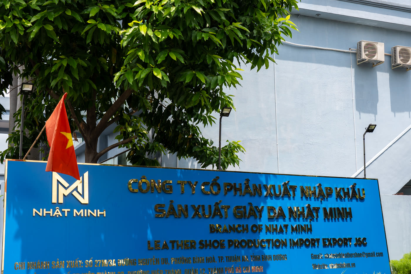 The company signboard at the plant entrance under a tree, with the national flag beside it.