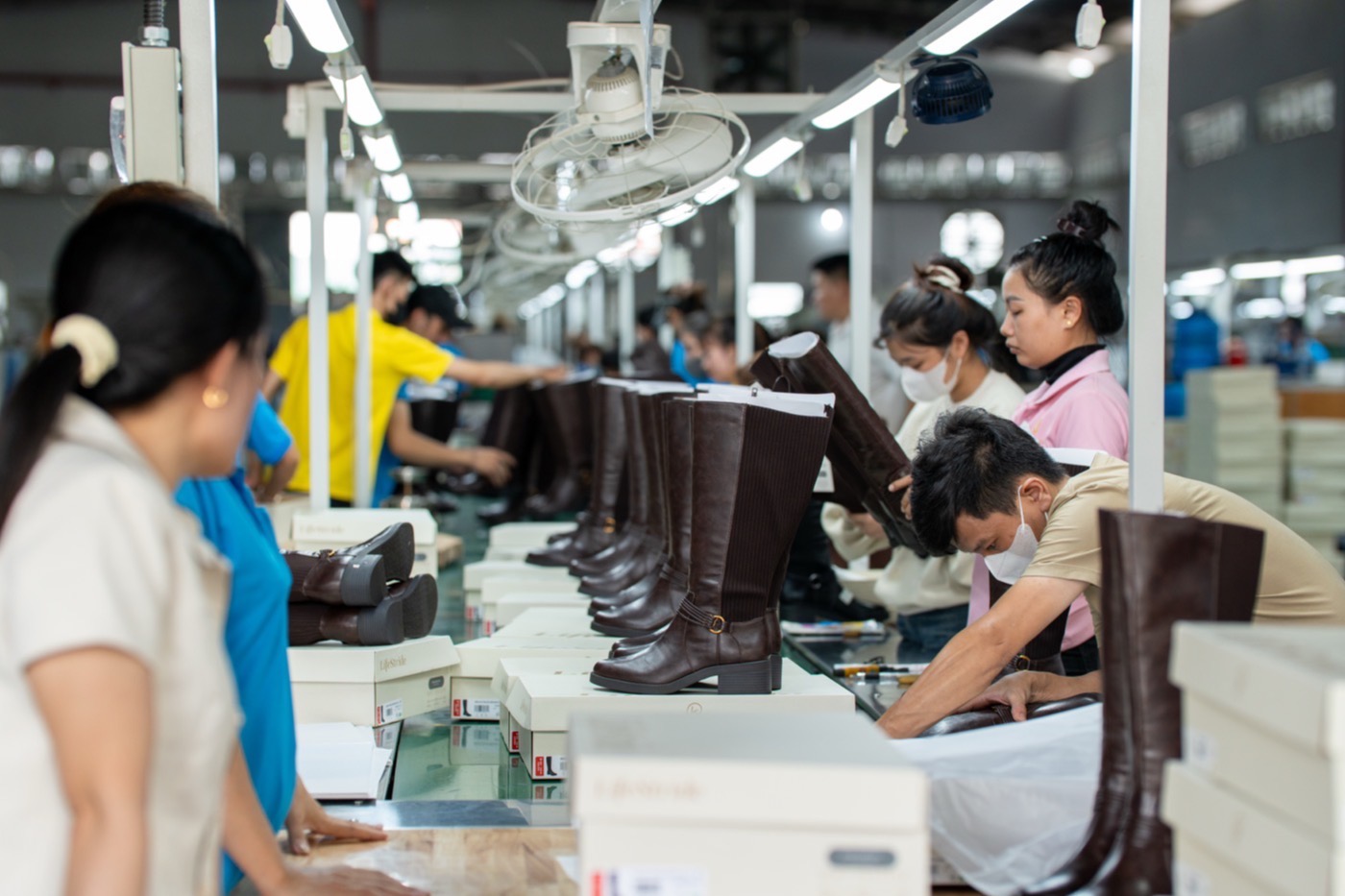 Finished leather boots standing in a row along the packing line, with boxes stacked beside them.