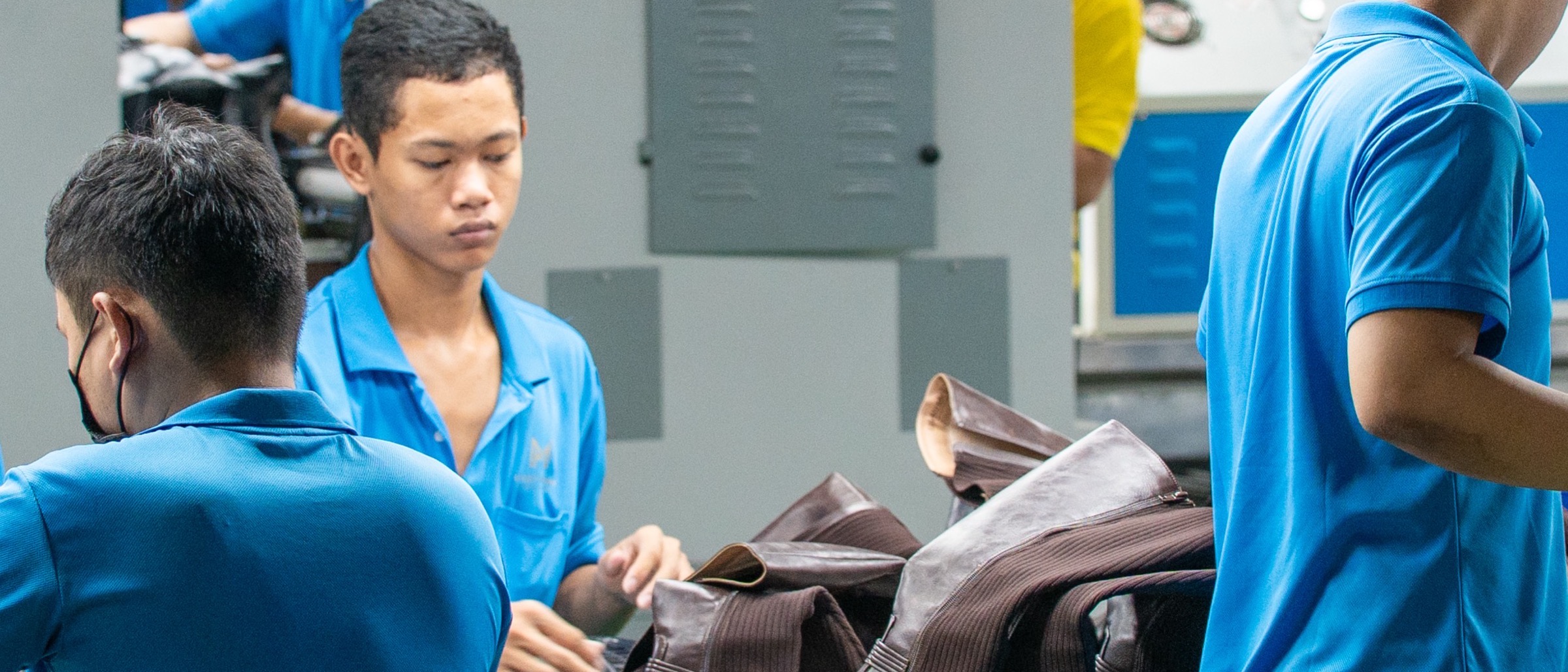 Three workers at a bench passing dark leather uppers along the assembly line.