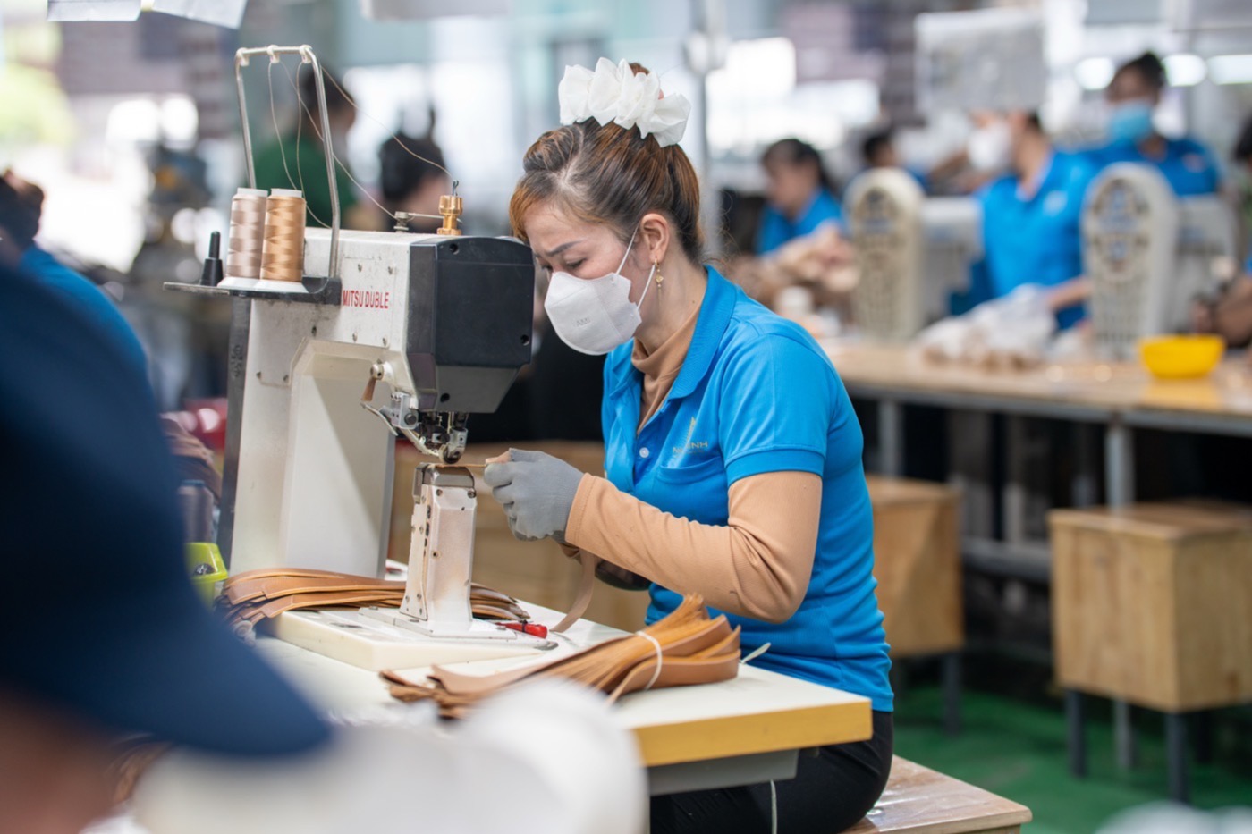 A machinist guiding a strip of tan leather under the needle of a closing machine.