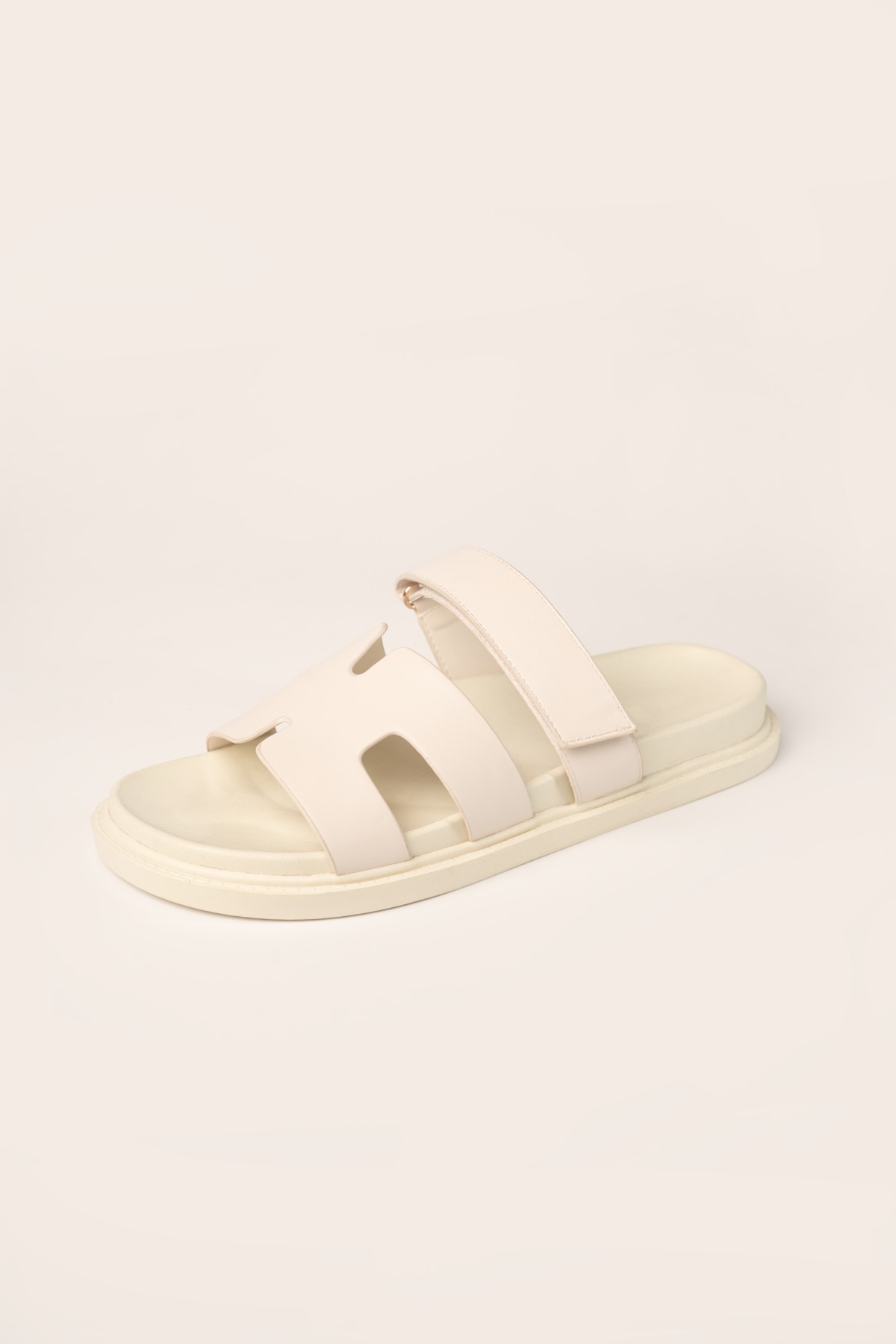 Studio shot of a cream flat slide sandal with a cut-out front band and adjustable instep strap.