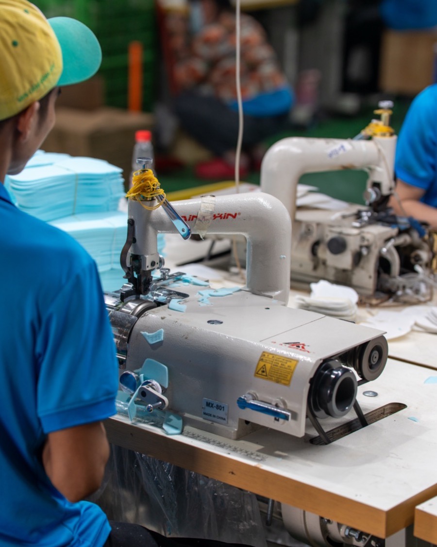 A single-purpose stitching machine in the closing room, with a stack of cut panels beside it.