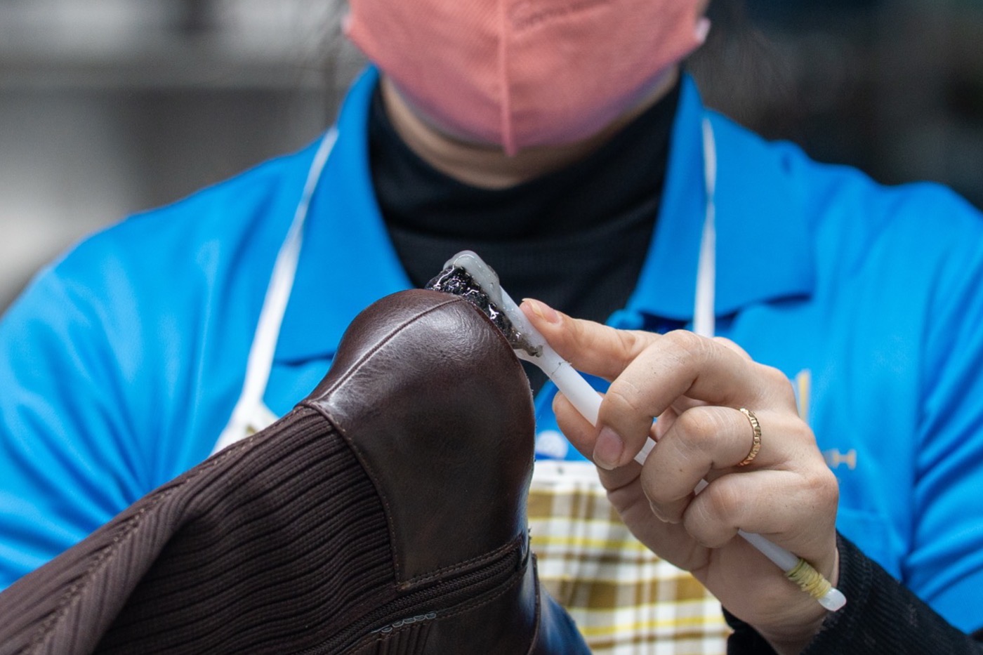 Hands at the finishing bench working over a dark leather boot.