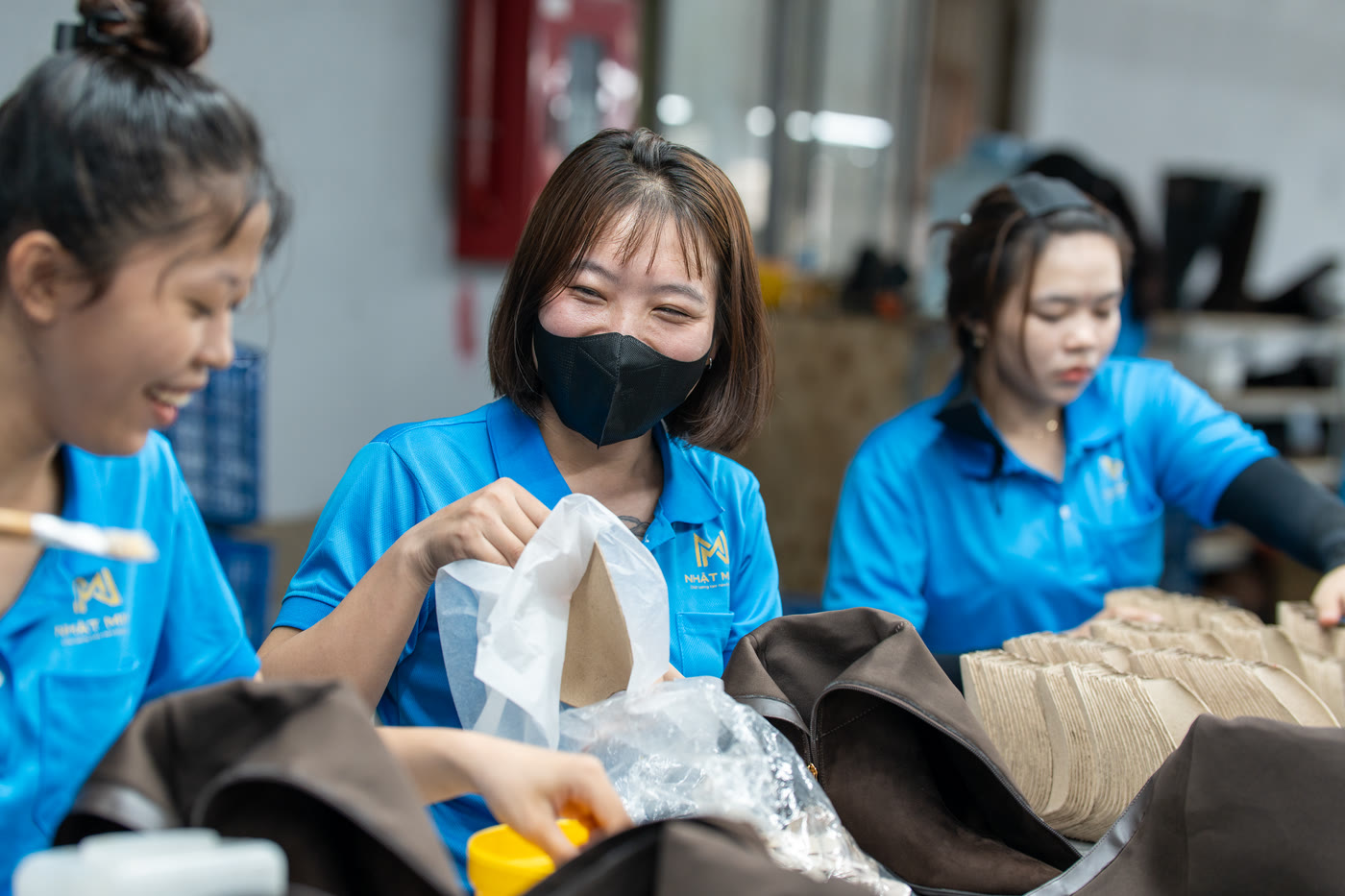 Three colleagues at a packing bench, bagging finished uppers.