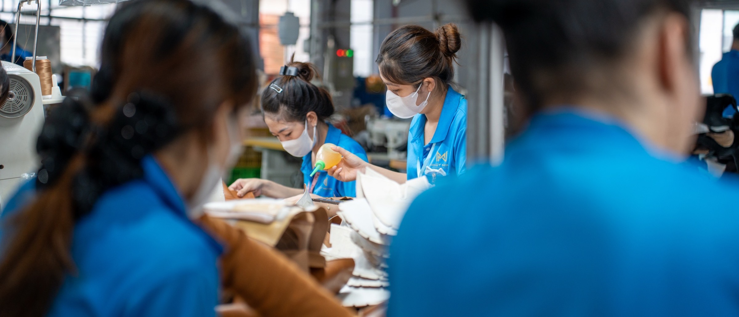 Women at the closing benches working along the line, cut panels stacked between them.