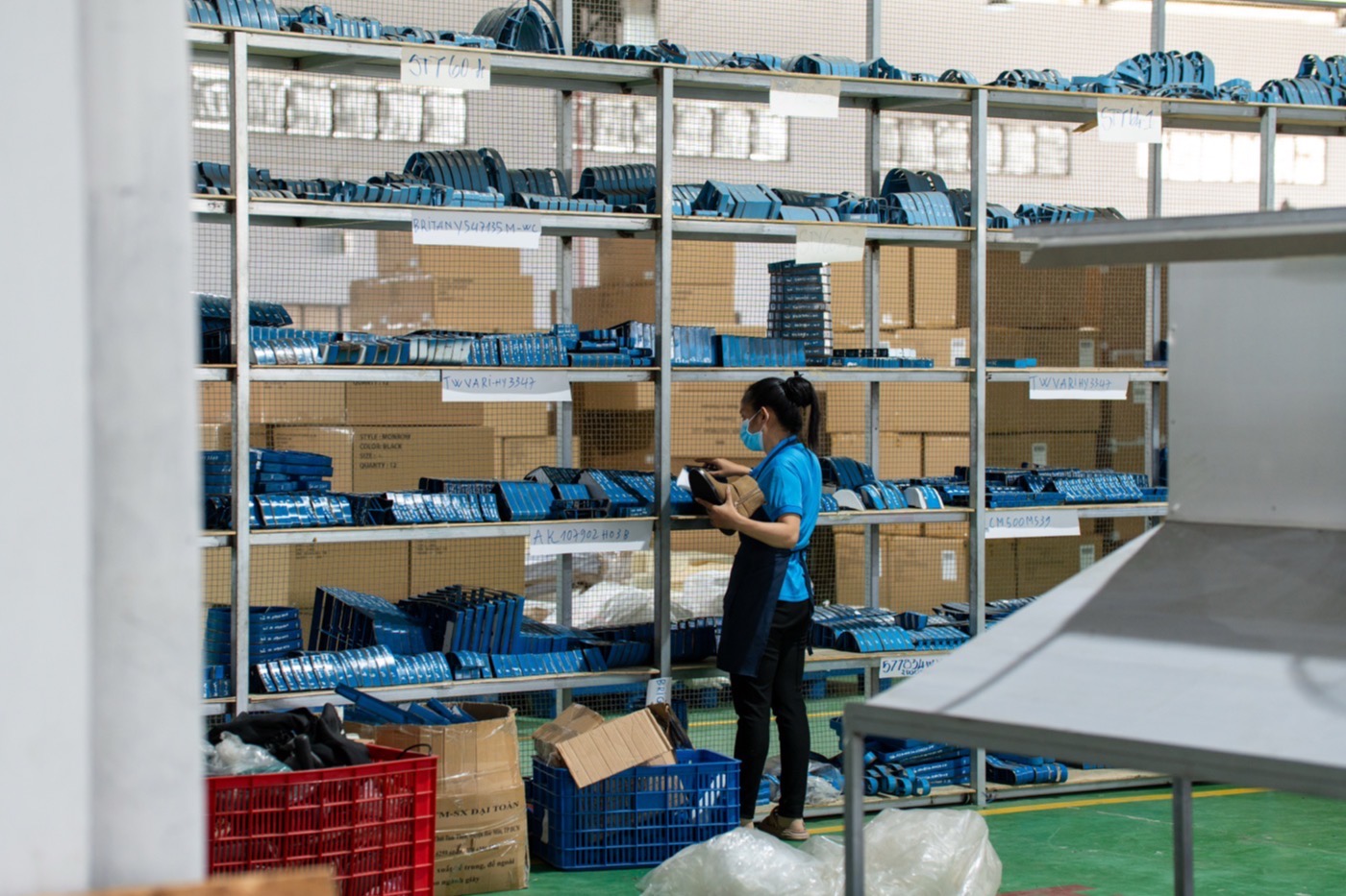 A worker checking stock against racked shelves of bagged and boxed components in the materials store.